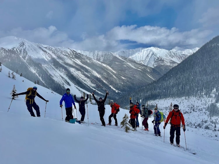 10 backcountry skiers posing and celebrating on a snowy slope with mountains in background