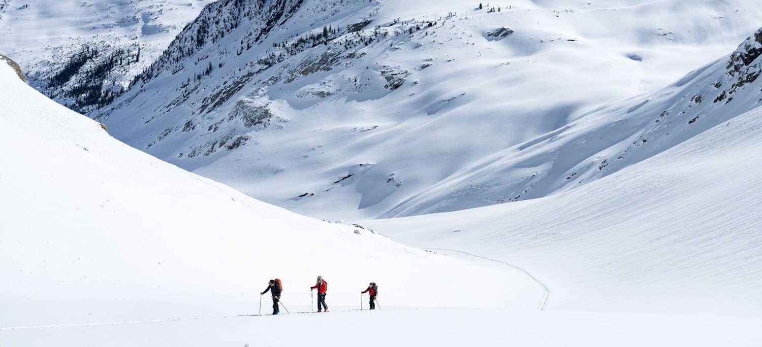 3 backcountry skiers on mountainous backdrop