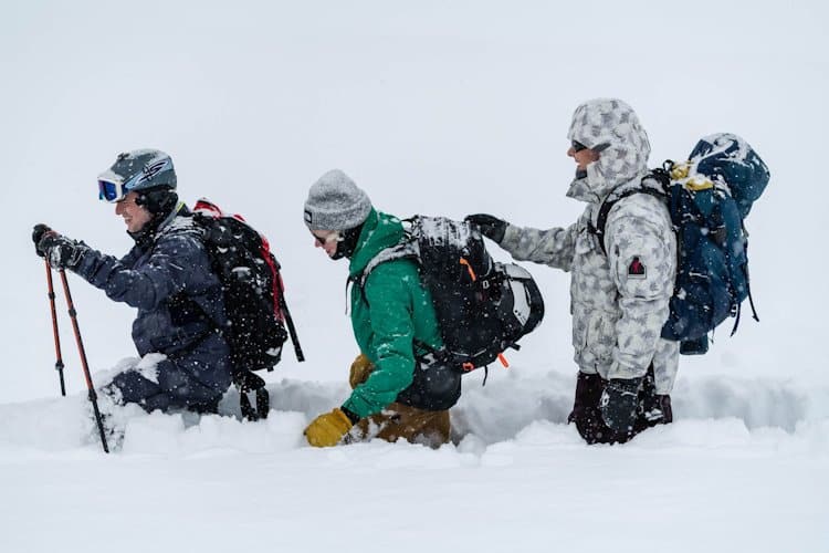 three people one behind another trudging through deep snow