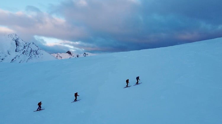 four backcountry skiers climbing up slope on slightly cloudy day