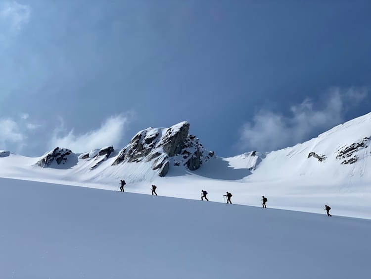 6 backcountry skier silhouette against snow cliff and blue skies