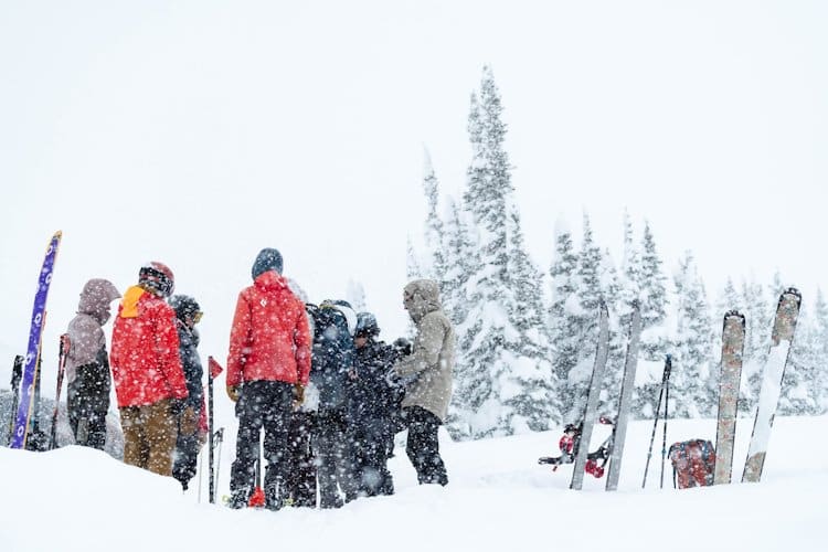 About seven people huddled together in the wintry outdoor with snow falling from sky