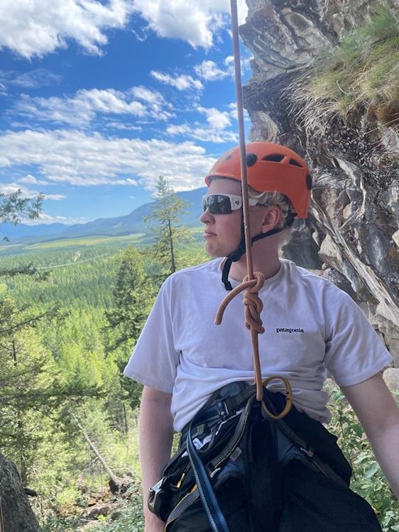 Helmeted climber tethered on rope outside near cliff during summer