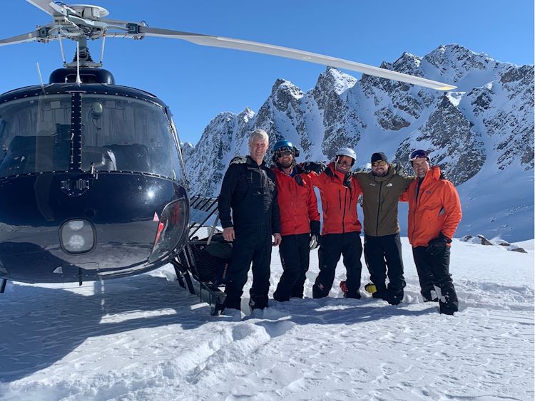 Parked helicopter and five men posing beside and snowy mountains in the background