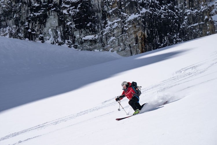 telemarking skier going down snowy slope with rocky background