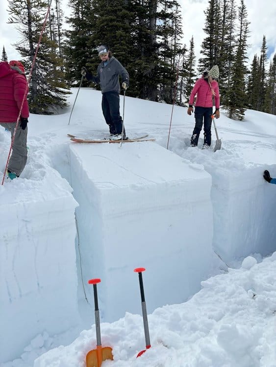 3 people standing on deep packed snow near trench showing depth of snowpack