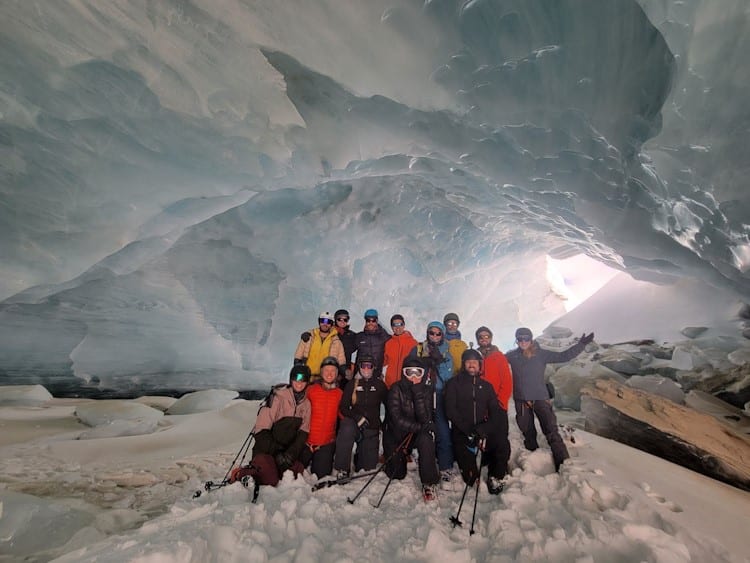 13 winter enthusiasts inside an ice cave with neat ceiling and snowy ground