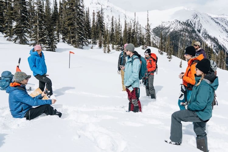 Seven winter hikers listening on one person sitting on snowy spot in the forest