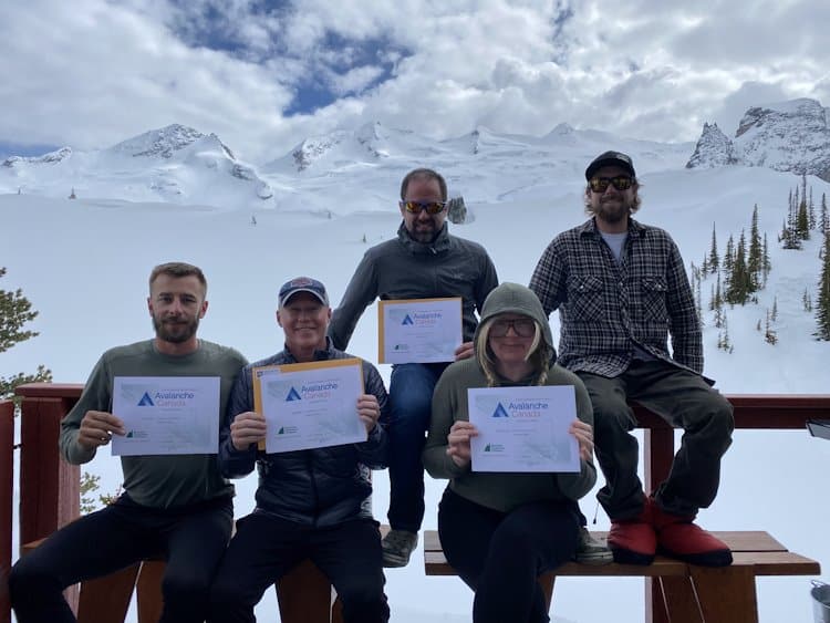 4 participants holding their Avalanche Skills Training course certificates and standing next to our founder, Tyson Retti. Impressive glaciers and large alpine slopes fill the background.