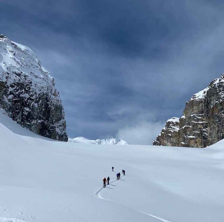 A group of participants and volunteers skinning up a open glaciated slope between two massive rock walls.