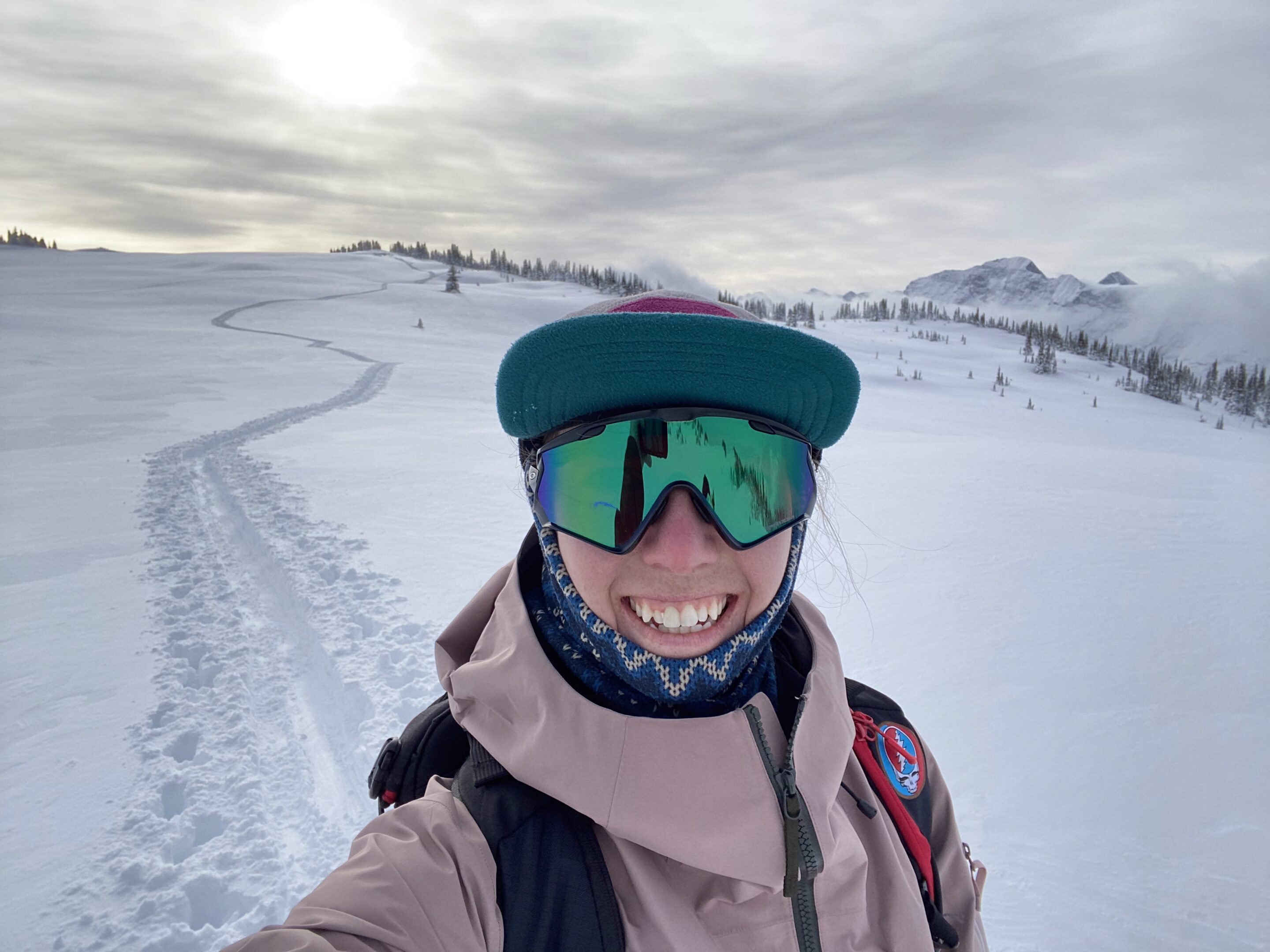 Kate smiles while out skiing. She is wearing tinted sunglasses and a sun hat and has a huge smile on her face. Kate is a caucasian female in her early-30s.