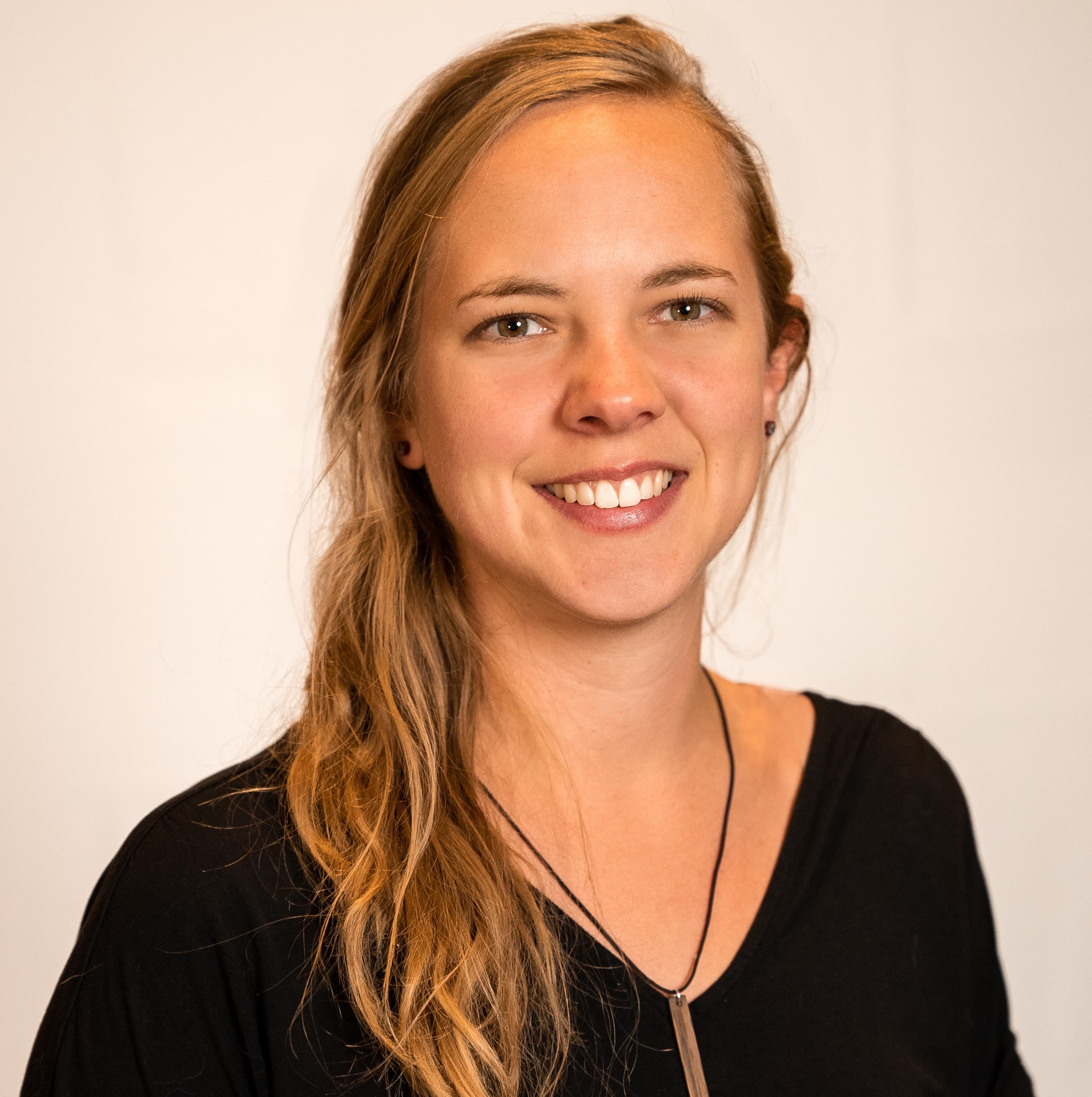 Lisa's professional headshot. She is wearing a black t-shirt, wooden pendant necklace, and is a 30-year-old female with blonde wavy hair.