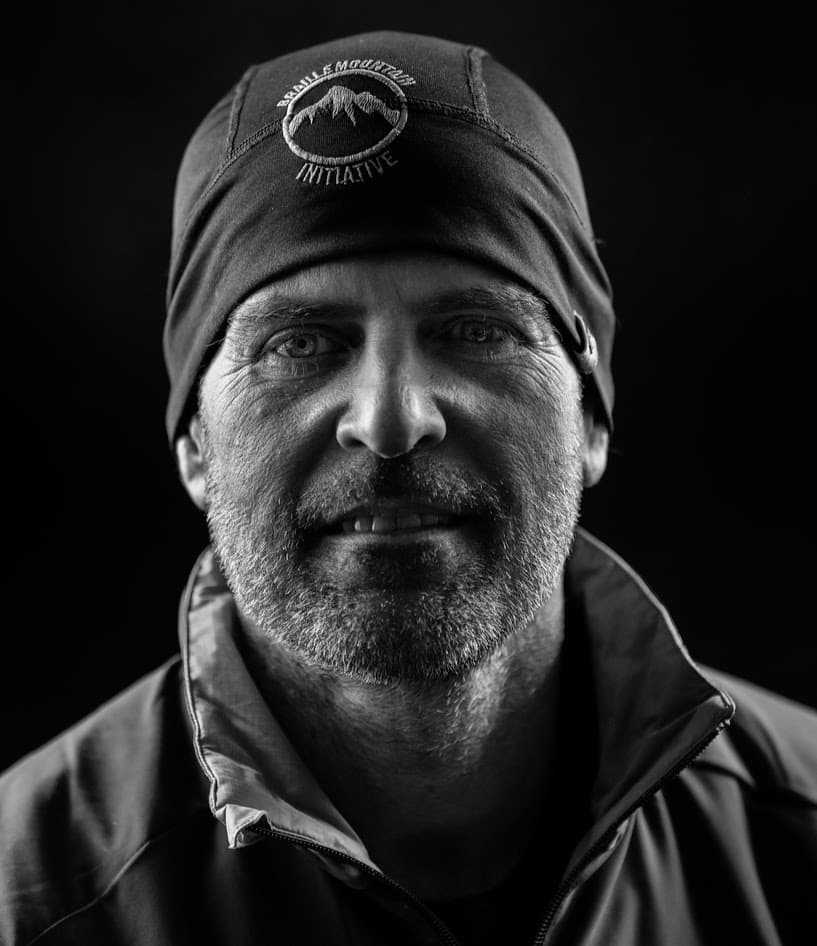 Mark's black-and-white headshot - he is wearing a black Braille Mountain toque. Mark is caucasian, in his mid-late 50s, and has stubble for facial hair.