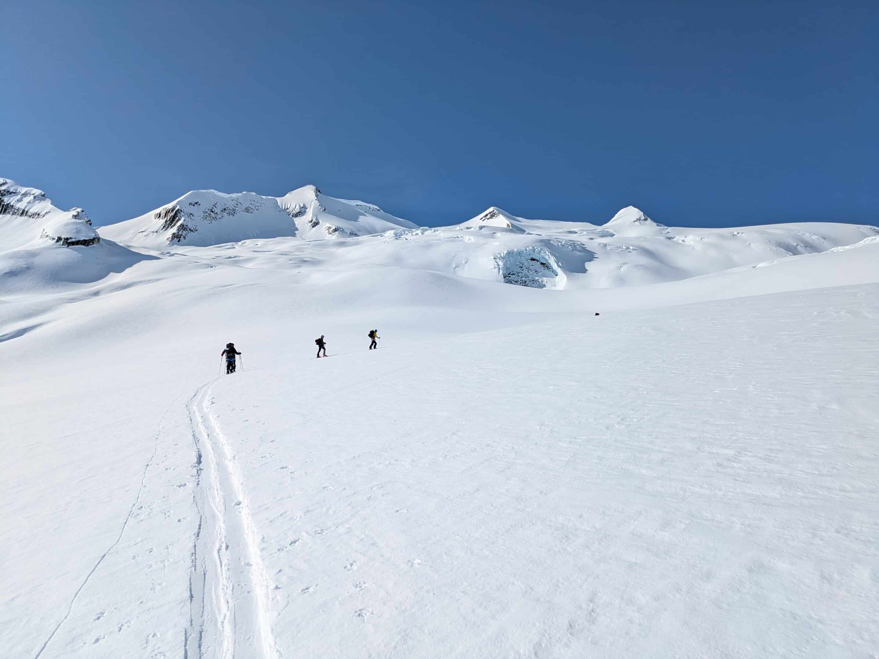 A group of ski tourers are skinning up a glaciated slope in a single-file line,