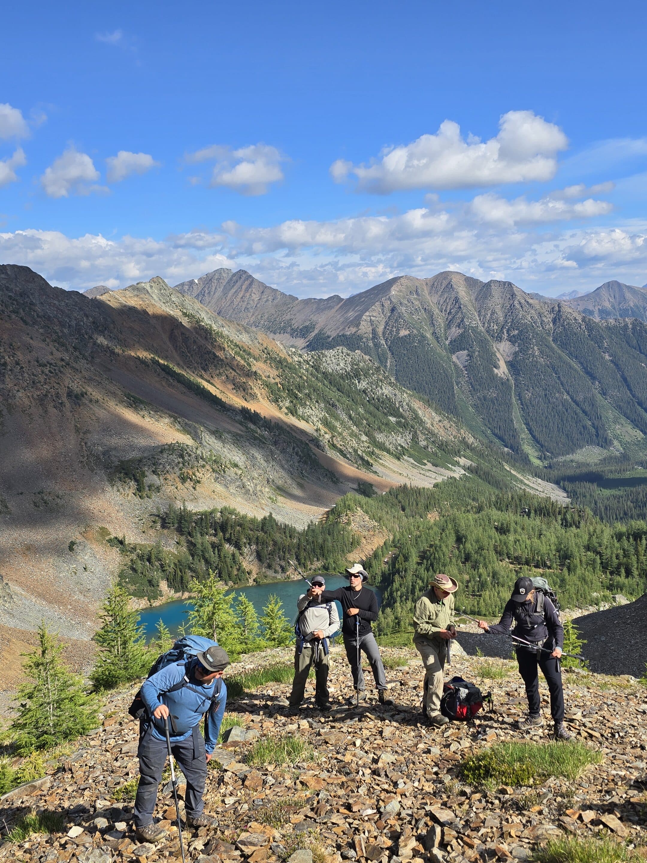 Seven people stand in a line on a skin track, spaced out for glacier travel, taking a quick break as they skin their way up Escargot Glacier.