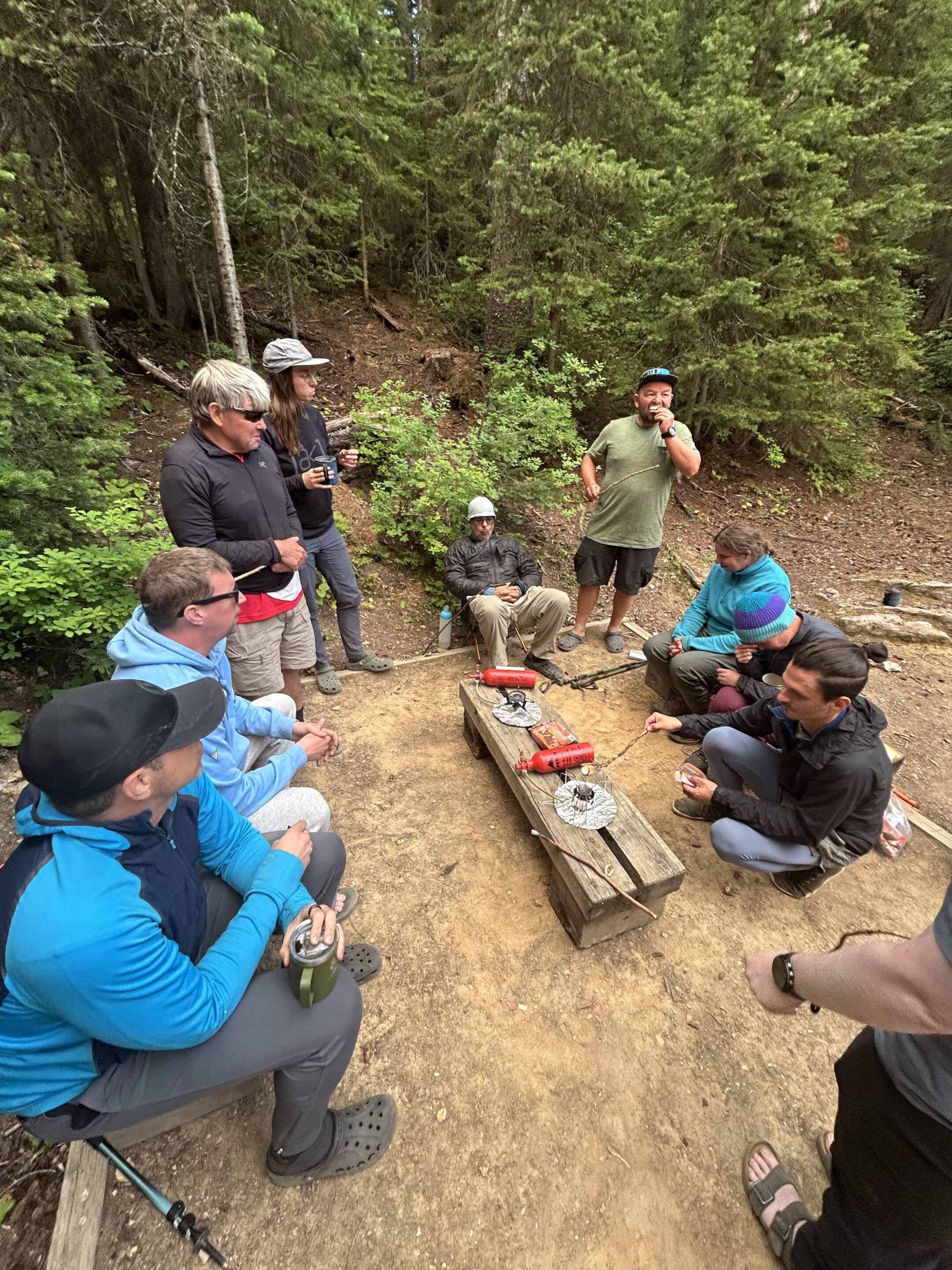 Ten people sit in a circle around camp cookware sharing their highs and lows from the day.