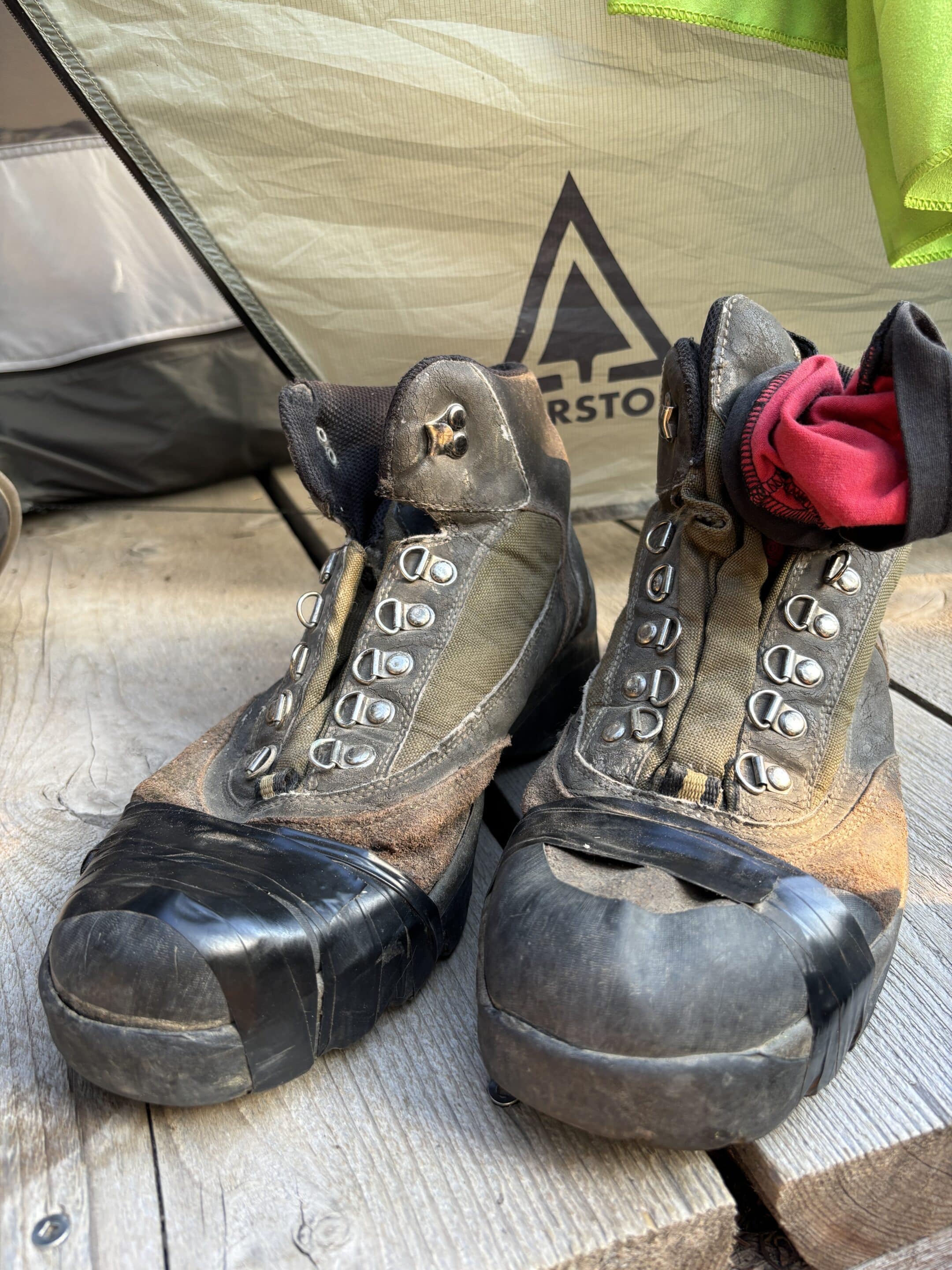 A pair of mens leather hiking boots are taped up across the toe area with black electrical tape.